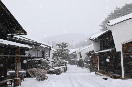 雪が降る古い街並みの写真です。雪で覆われた道沿いに、木造の家屋が並んでいます。