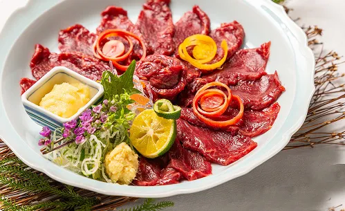 赤身の馬刺しが円形に盛り付けられた一皿。すだちや薬味が添えられ、彩り豊かなパプリカと玉ねぎが飾られている。