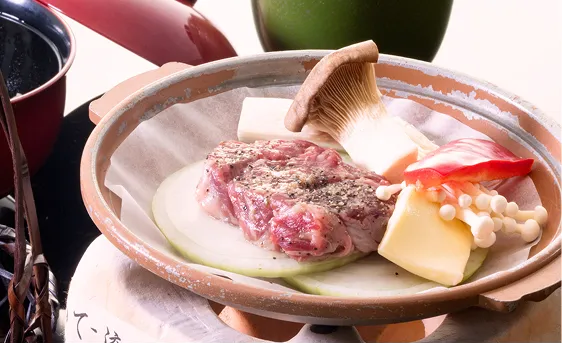 一人用の土鍋に入った、牛肉と野菜の盛り合わせ。牛肉は黒胡椒が振られ、エリンギ、豆腐、エノキ、玉ねぎが添えられている。