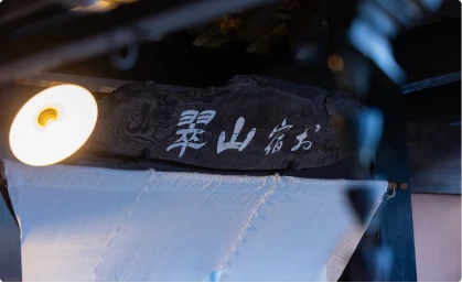 木製の看板に白い文字で「お宿 山翠」と書かれている。