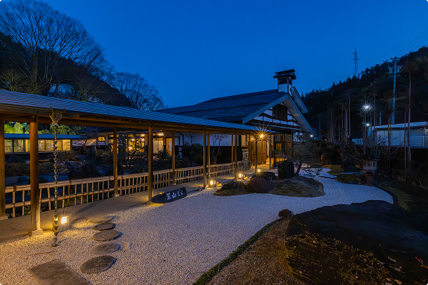 夕暮れ時の翠天 天上の庭。ライトアップされた建物と庭園が幻想的な雰囲気を醸し出す。落ち着いた光が石畳の小道を照らし、奥へと続く。静寂に包まれた、和の趣を感じる空間