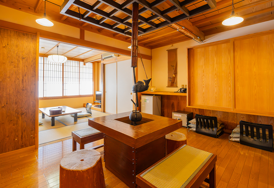 中央には囲炉裏があり、その上には自在鉤にかけられた茶釜が吊るされています。床は光沢のある木製で、畳敷きの小上がりには座卓と座椅子が置かれています。