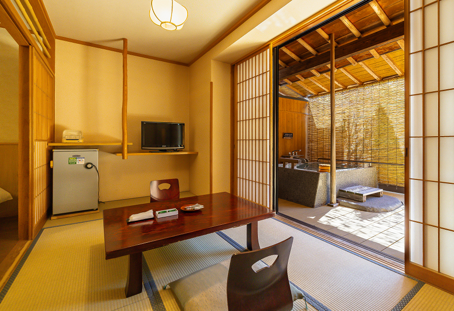 畳敷きの部屋に置かれた落ち着いた雰囲気のテーブルと椅子。奥には障子で仕切られた露天風呂があり、竹で編まれた目隠しが風情を感じさせる。